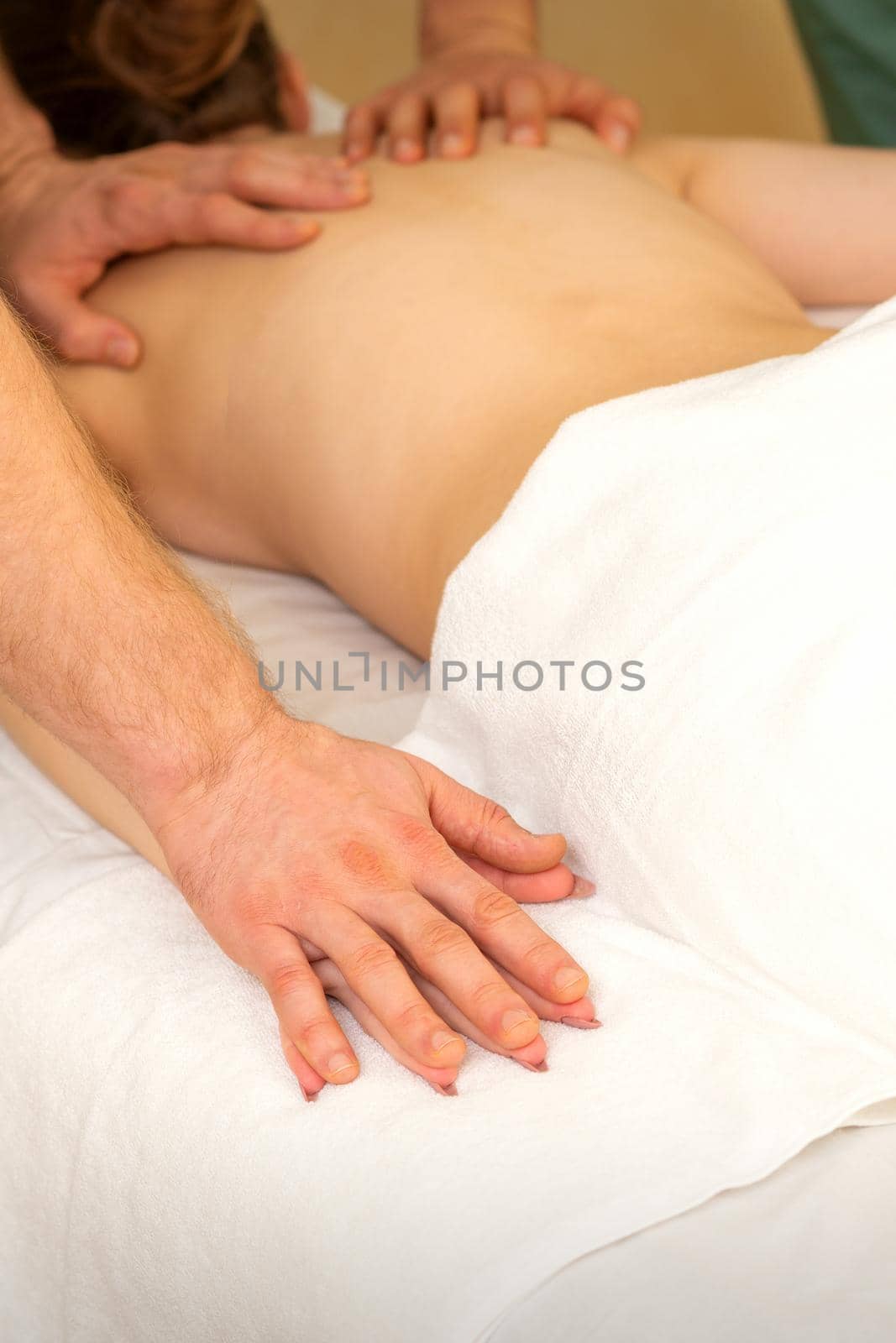 Back and hands double massage with four hands of two professional massagers for a young caucasian woman in a spa salon