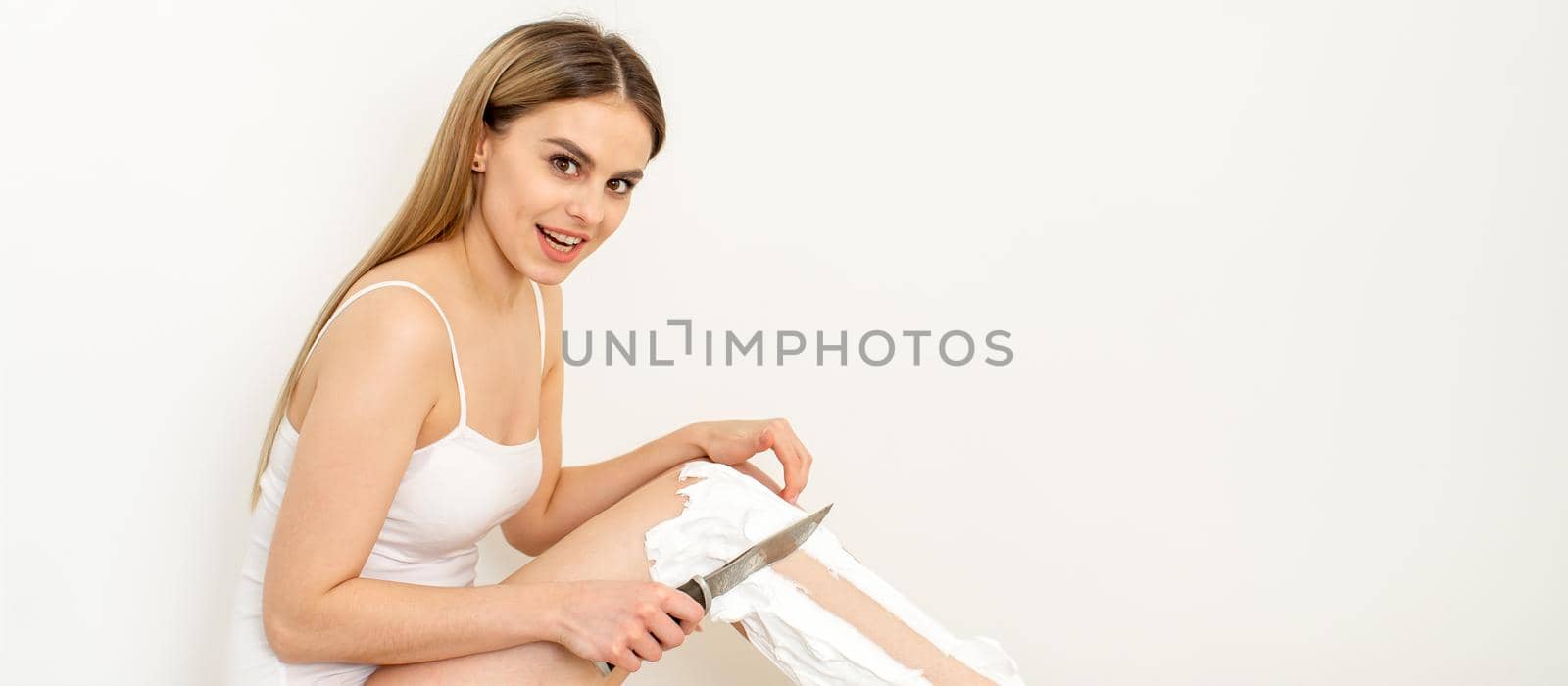 Beautiful caucasian woman shaving her legs with a knife with shaving foam on white background. Depilation and epilation concept