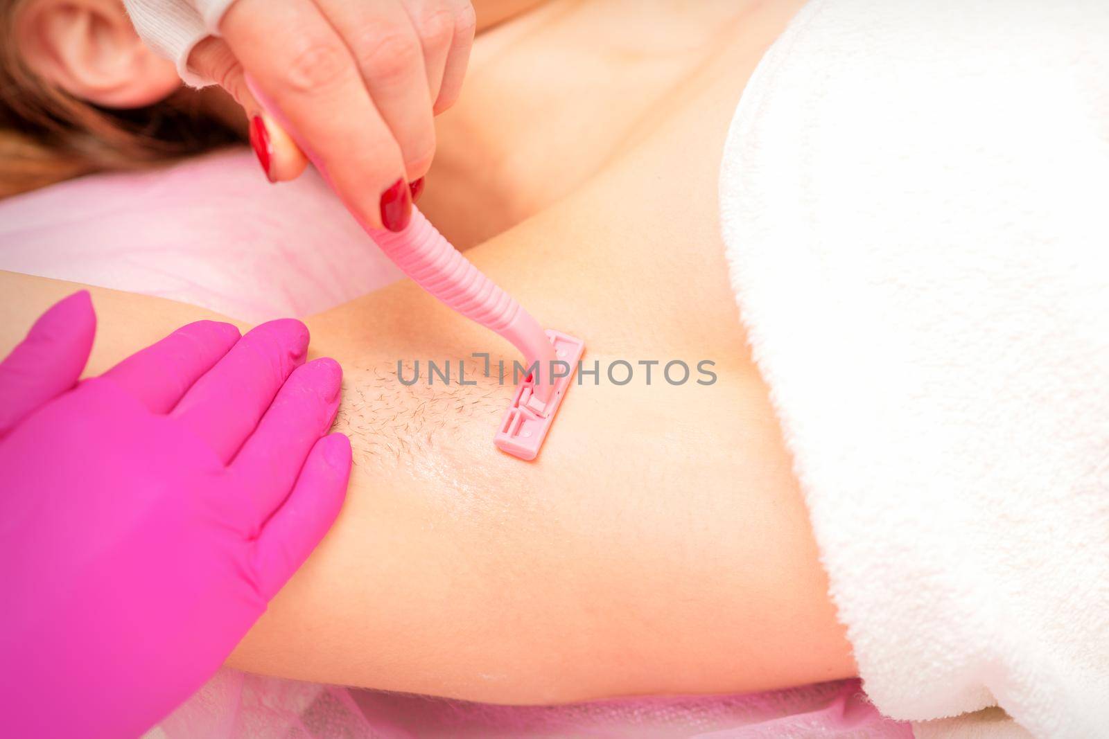 Beautician shaves the armpit of a young woman with a razor before the hair removal procedure