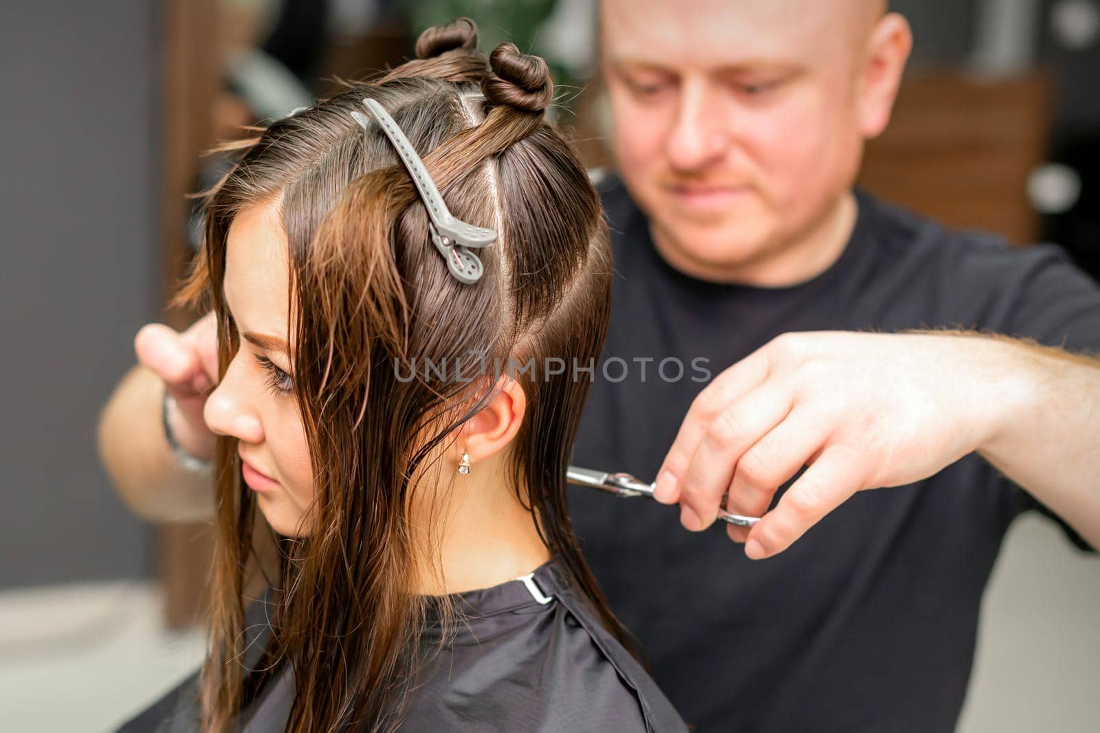 Male stylist cutting the hair of female client in professional beauty salon. by okskukuruza