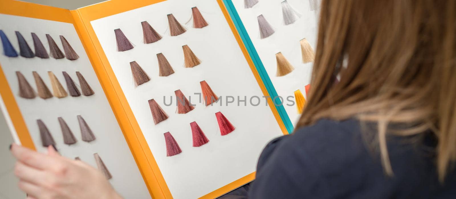 Young brunette woman choosing hair color from palette samples at the beauty salon, hair dyeing concept. by okskukuruza