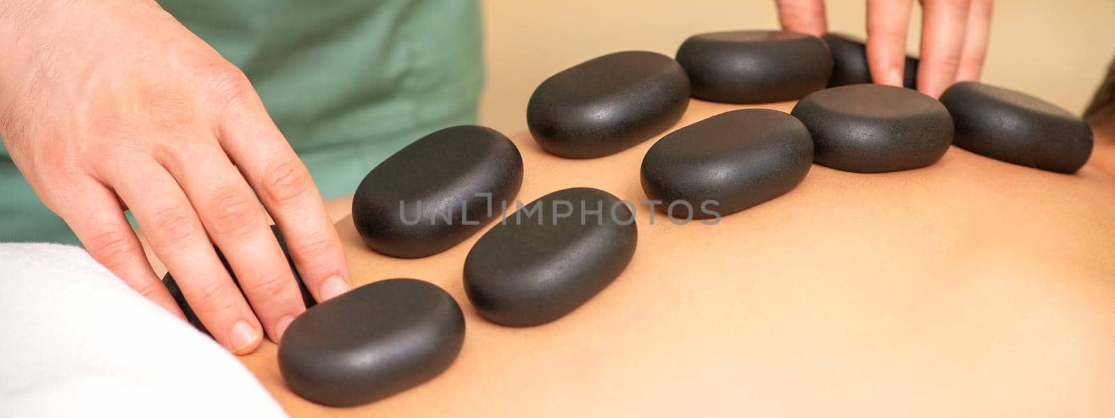 Young caucasian woman receiving back massage with black stones by masseur in spa salon. A woman getting a spa treatment