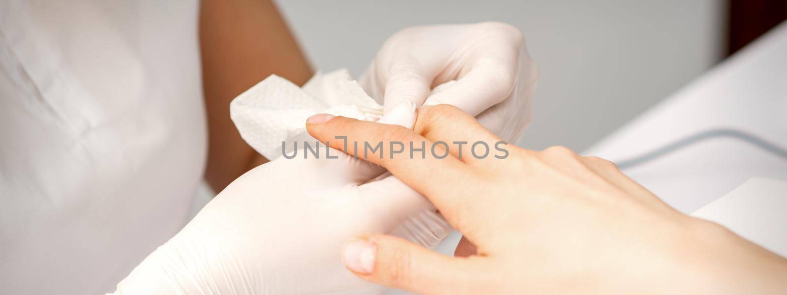 Manicure master wiping the moisturizer from the end of female fingers in beauty salon. by okskukuruza