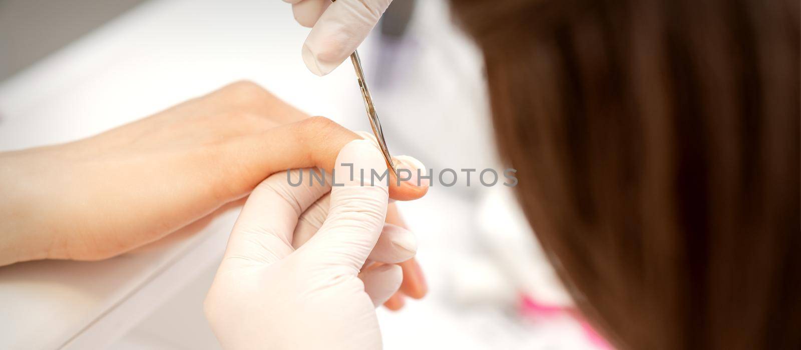 Close up of manicure master with manicure scissors removes cuticles on female nails at a beauty salon