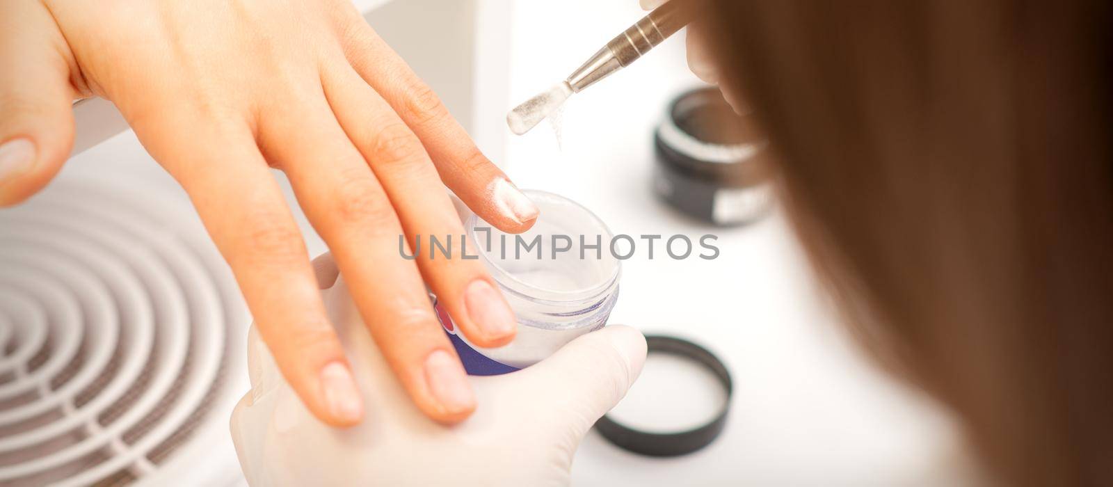 Manicure master applying acrylic powder on the female nails in a beauty salon. Strengthening of nails acrylic powder