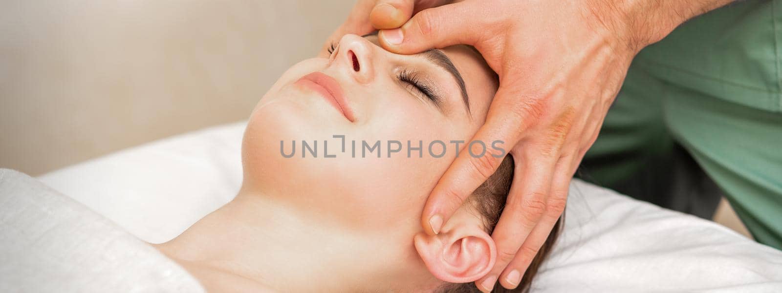 Pretty young caucasian woman receiving a head massage by a male massage therapist in a beauty salon