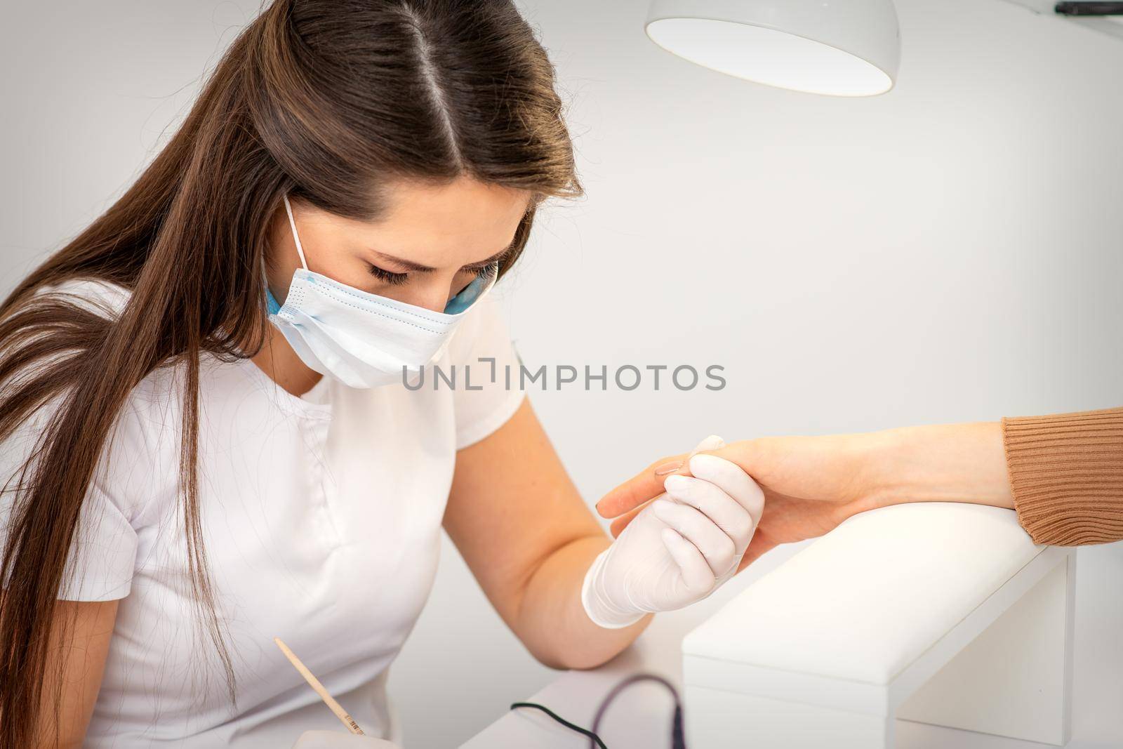 Manicure master with white protective mask painting female nails with nail polish in manicure salon