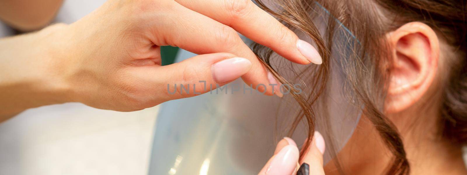 Close Up hairdresser stylist makes hairstyle for a young woman in a beauty salon. by okskukuruza