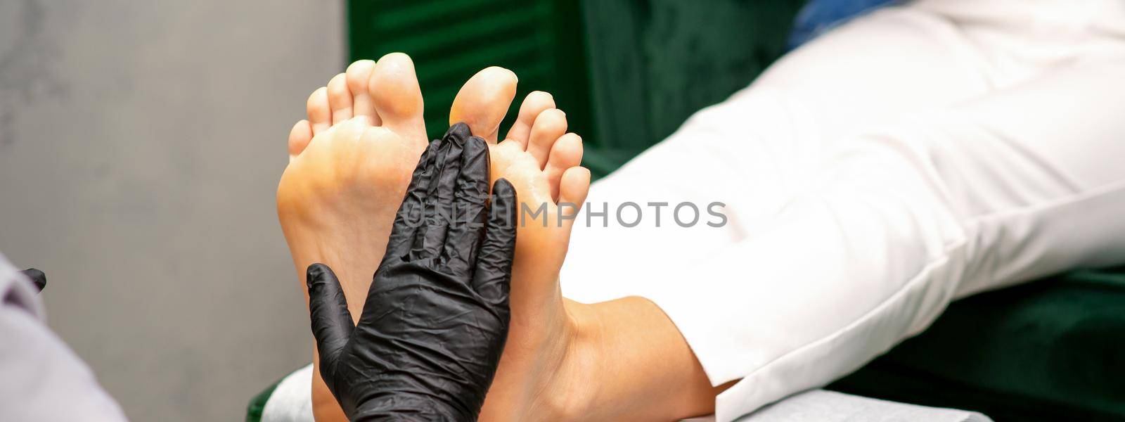 Moisturizing the feet. Hands of pedicure master in black gloves care about female feet. Foot massage. Pedicure beauty salon concept