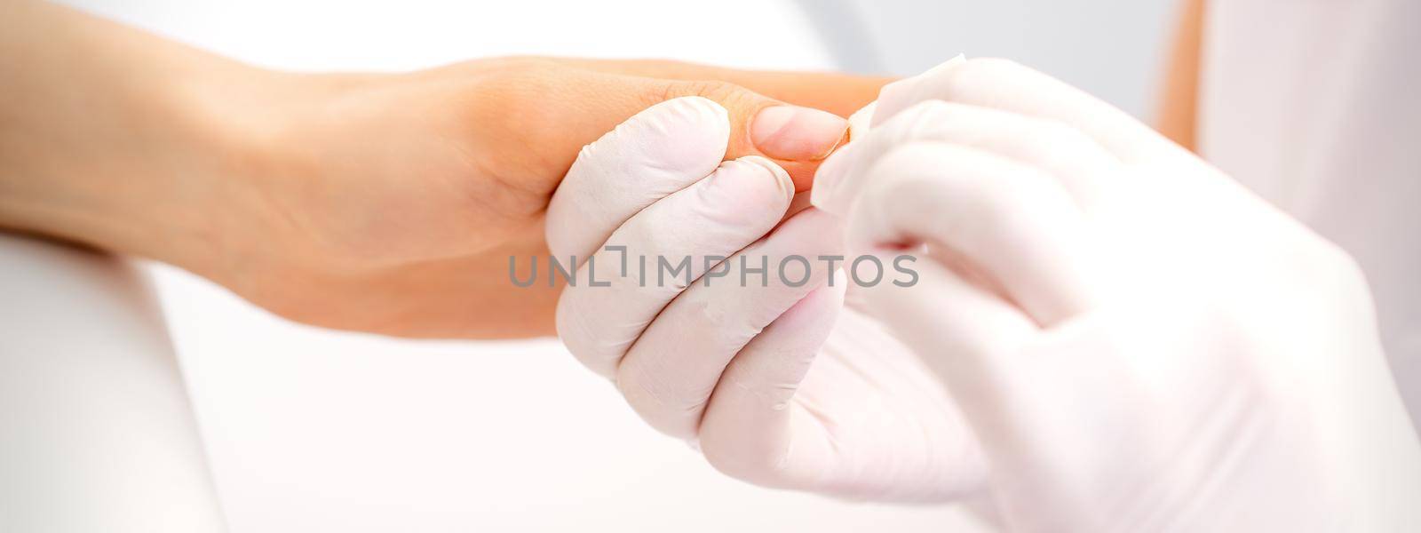 Manicure master wiping the moisturizer from the end of female fingers in beauty salon. by okskukuruza