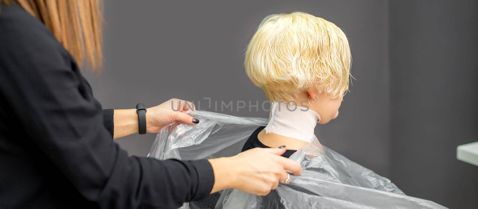 Hairstylist covers neck with cape for a female client in a beauty salon. by okskukuruza