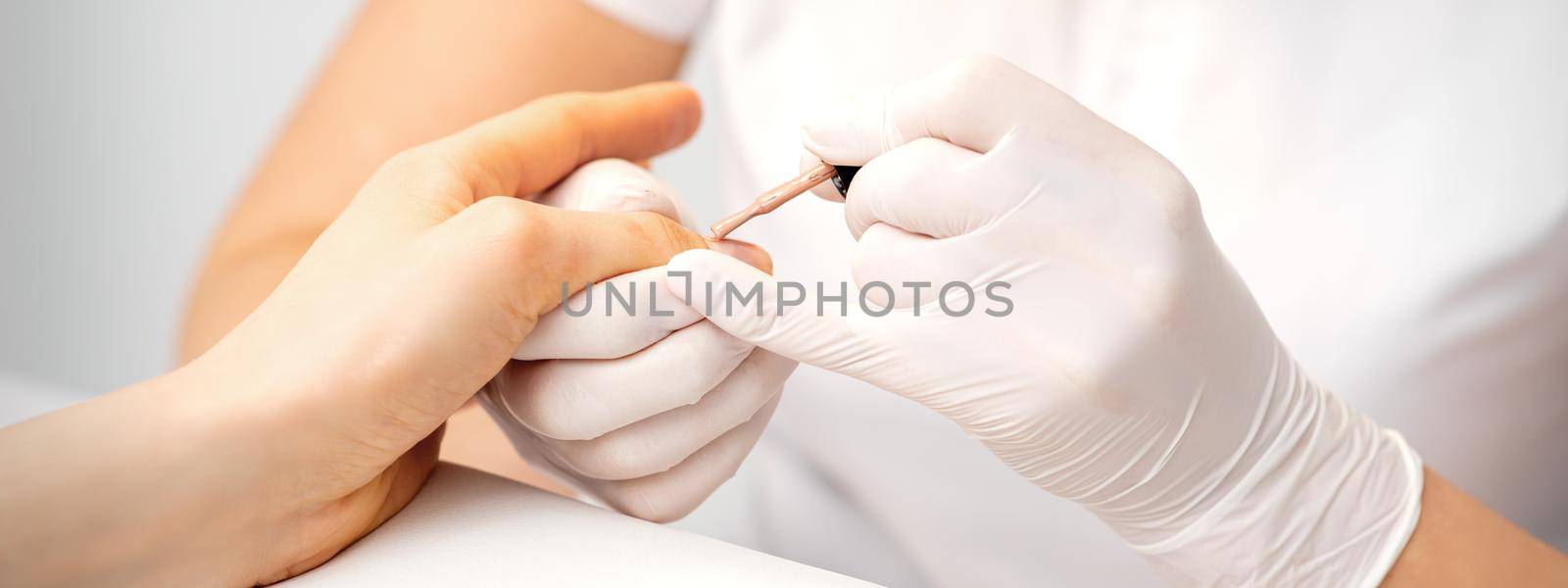 Young woman receiving pink or beige nail polish in a beauty salon