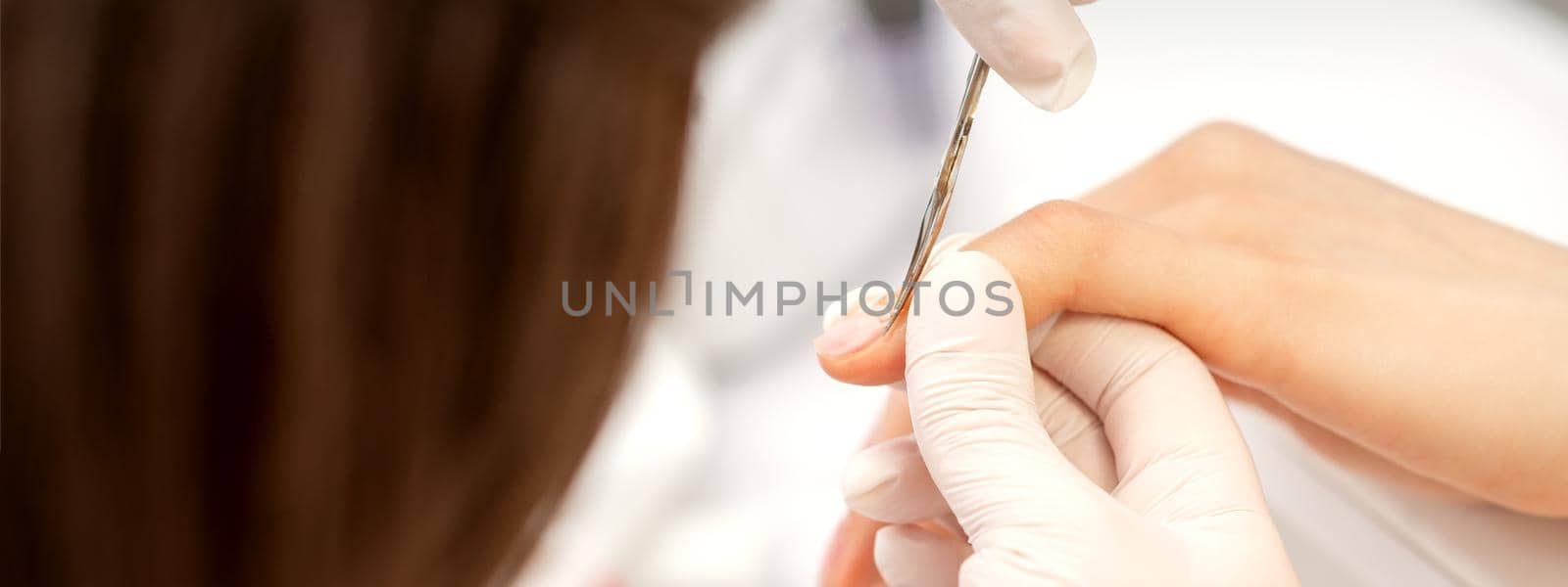 Close up of manicure master with manicure scissors removes cuticles on female nails at a beauty salon