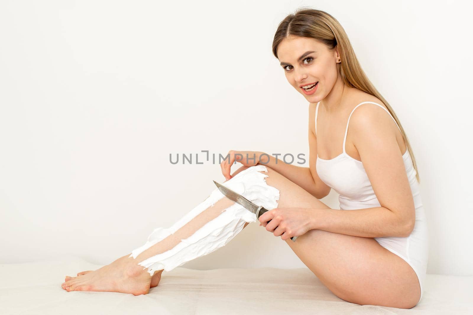Beautiful caucasian woman shaving her legs with a knife with shaving foam on white background. Depilation and epilation concept