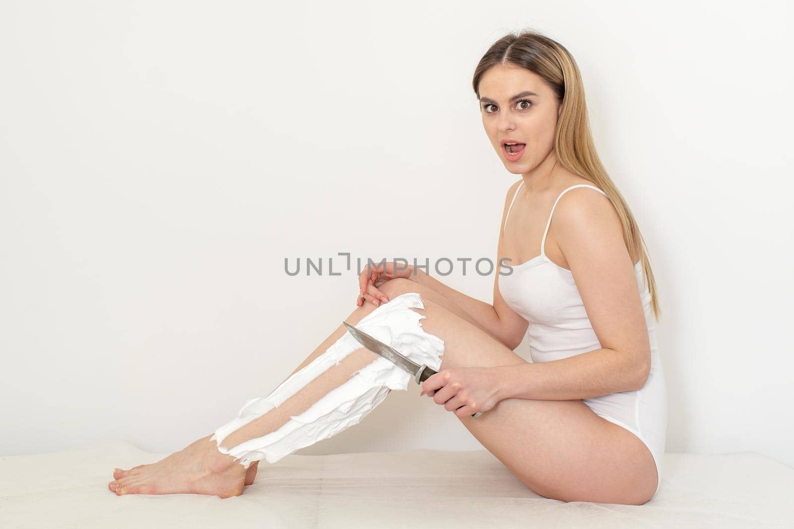 Beautiful caucasian woman shaving her legs with a knife with shaving foam on white background. Depilation and epilation concept