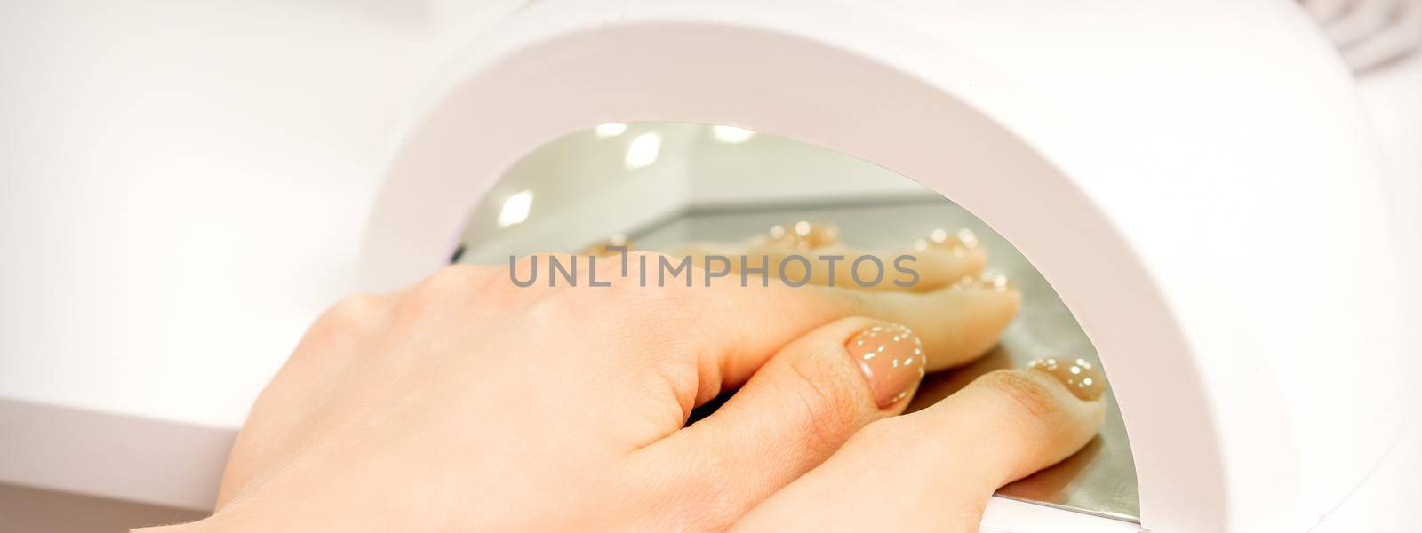 Female hand with manicured fingers dry inside UV light machine in manicure salon