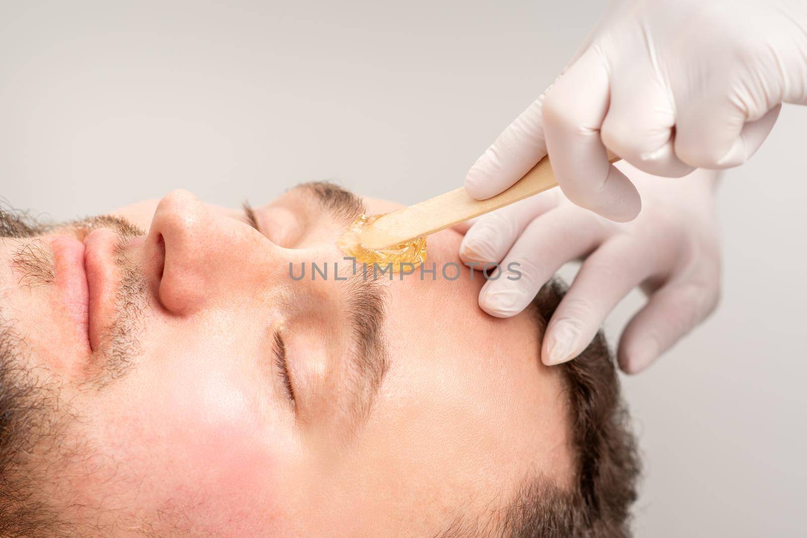 Beautician applying wax paste between eyebrows during the procedure of waxing in the beauty salon