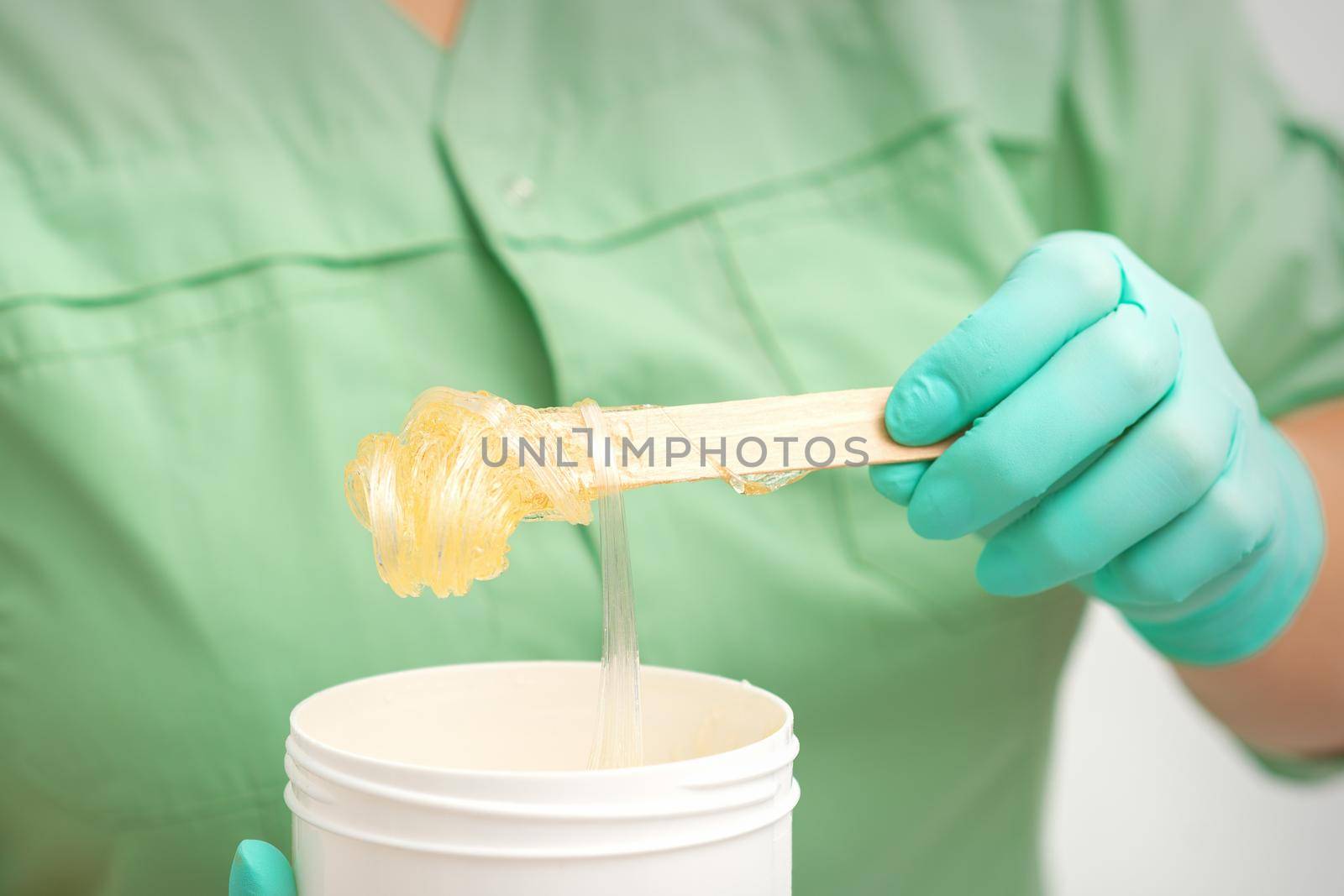 Liquid yellow sugar paste for depilation on a stick flows into the jar in hands of a beautician