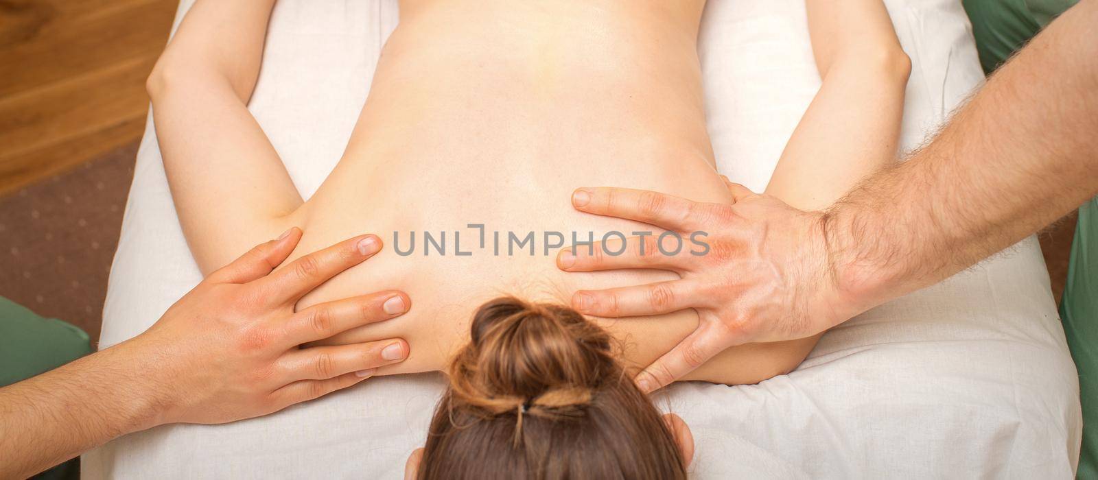 Back massage for a young woman with four hands in a spa