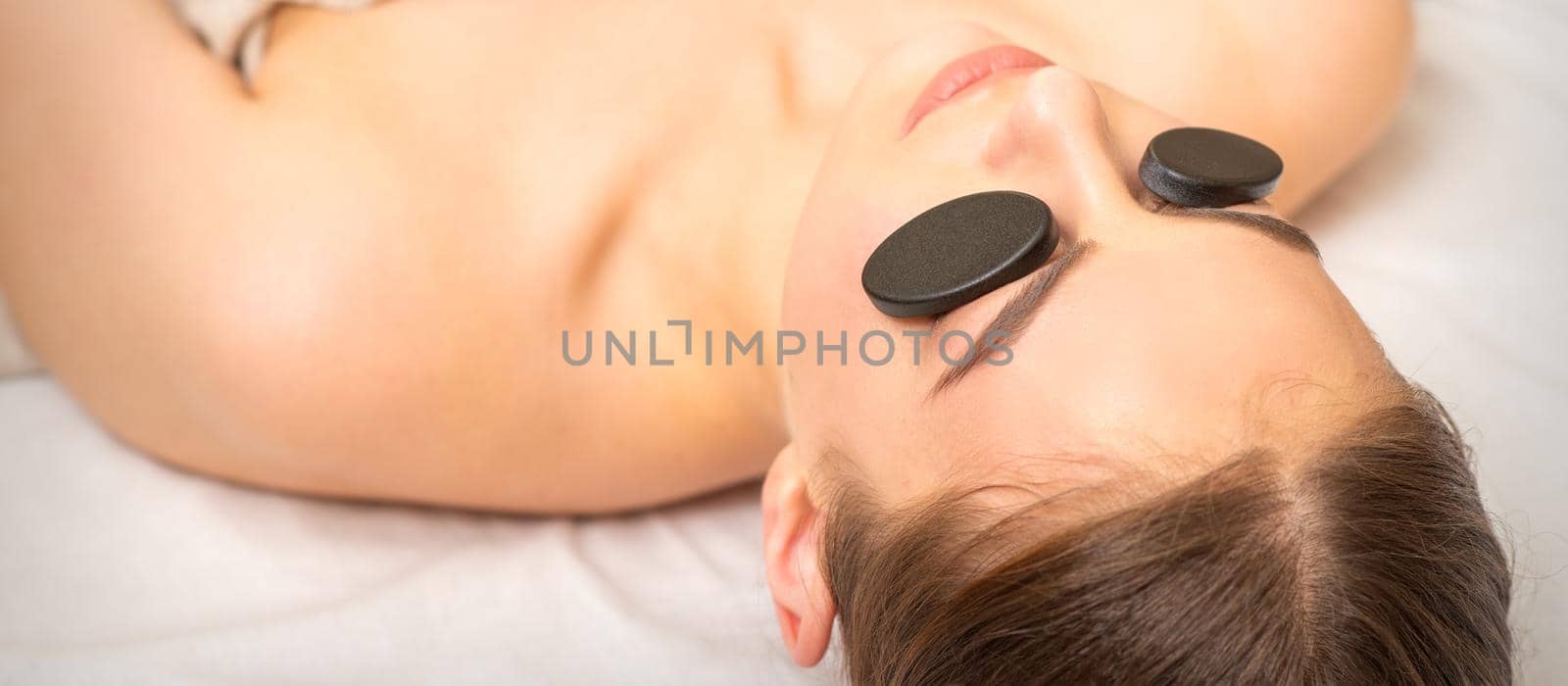 Massage with stones on the eyes of young woman getting a treatment in a beauty spa