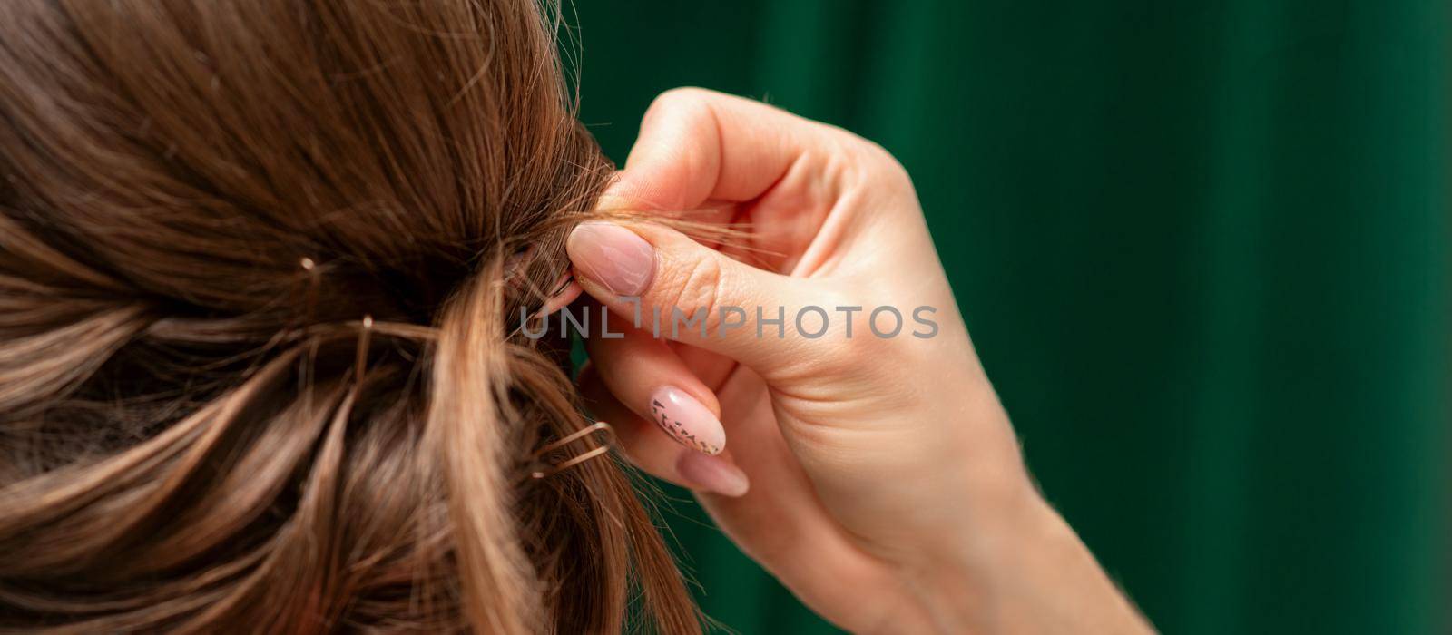 Hairdresser makes hairstyles for a young woman in beauty salon close up. by okskukuruza