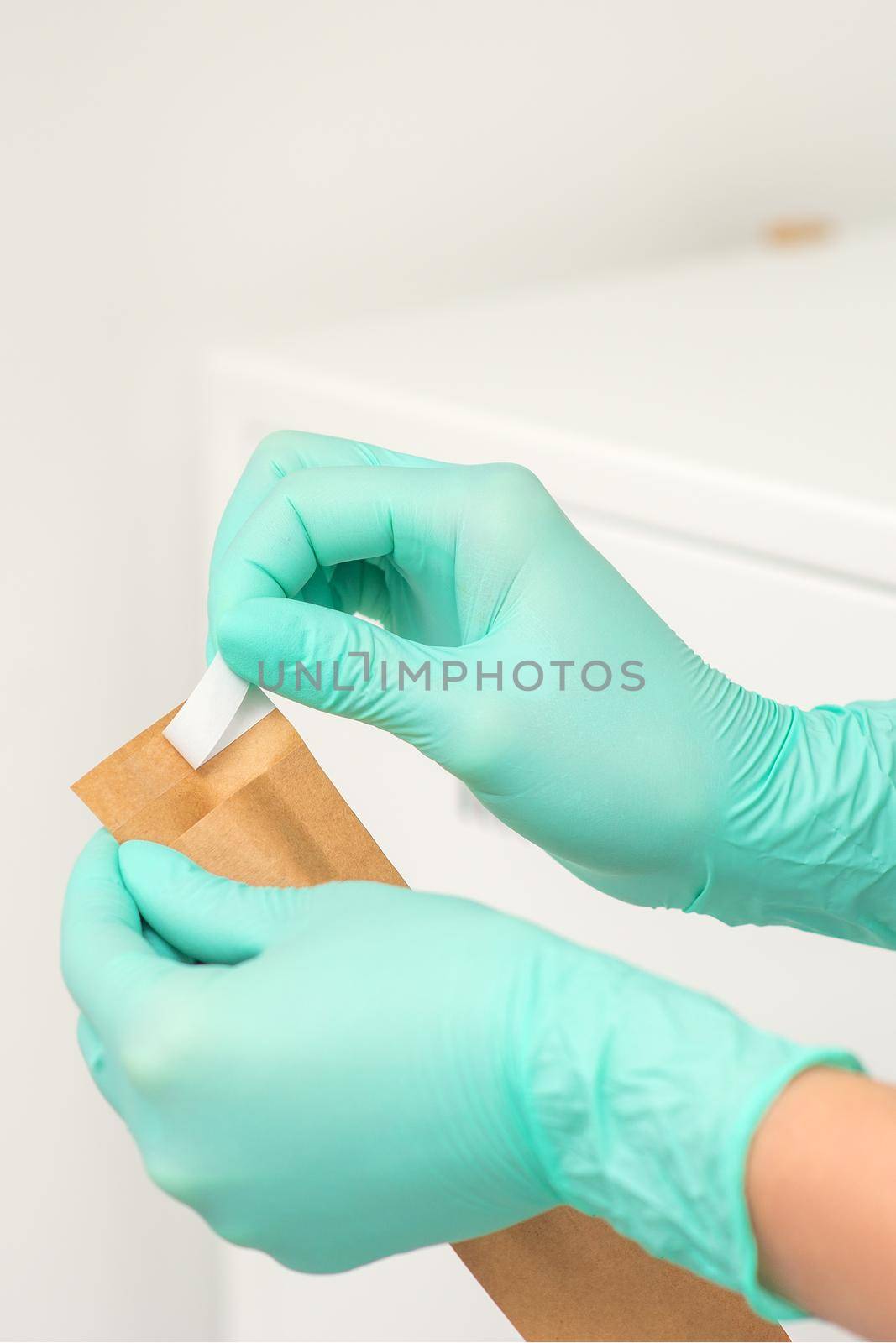 Beautician in green protective gloves holds a craft envelope to sterilize tools before disinfection