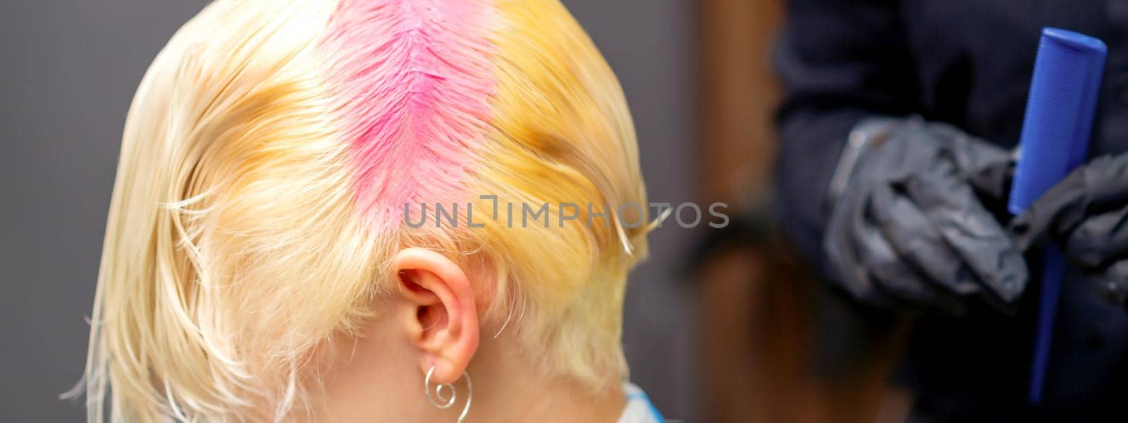 Young caucasian woman tints hair roots in pink color in a beauty salon