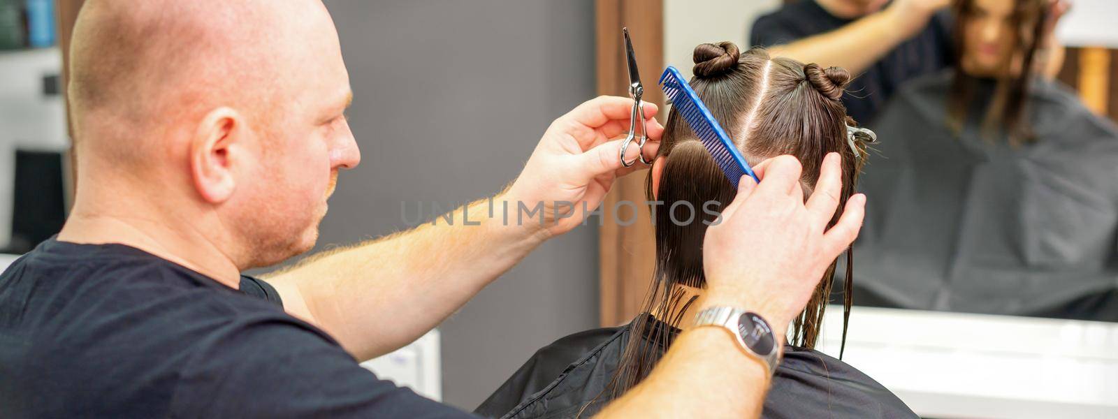 Male stylist cutting the hair of female client in professional beauty salon. by okskukuruza