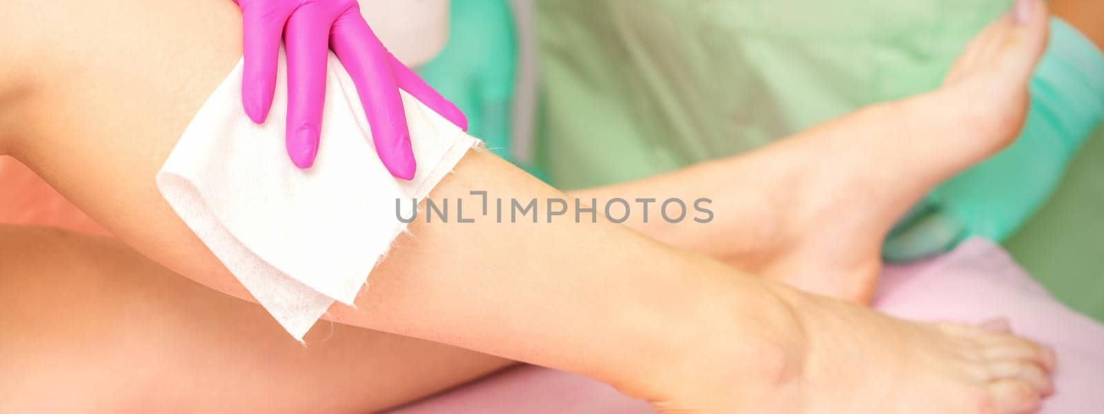 Master of depilation wipes female feet with white napkin preparing for the procedure of hair removal