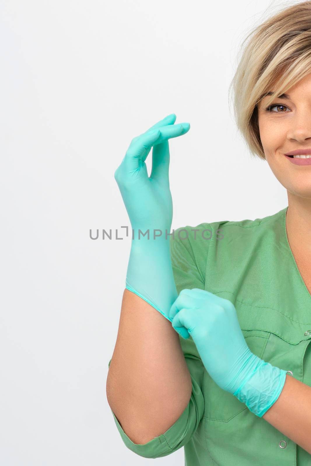 Doctor beautician puts on sterile blue gloves smiling prepares to receive clients on white. by okskukuruza