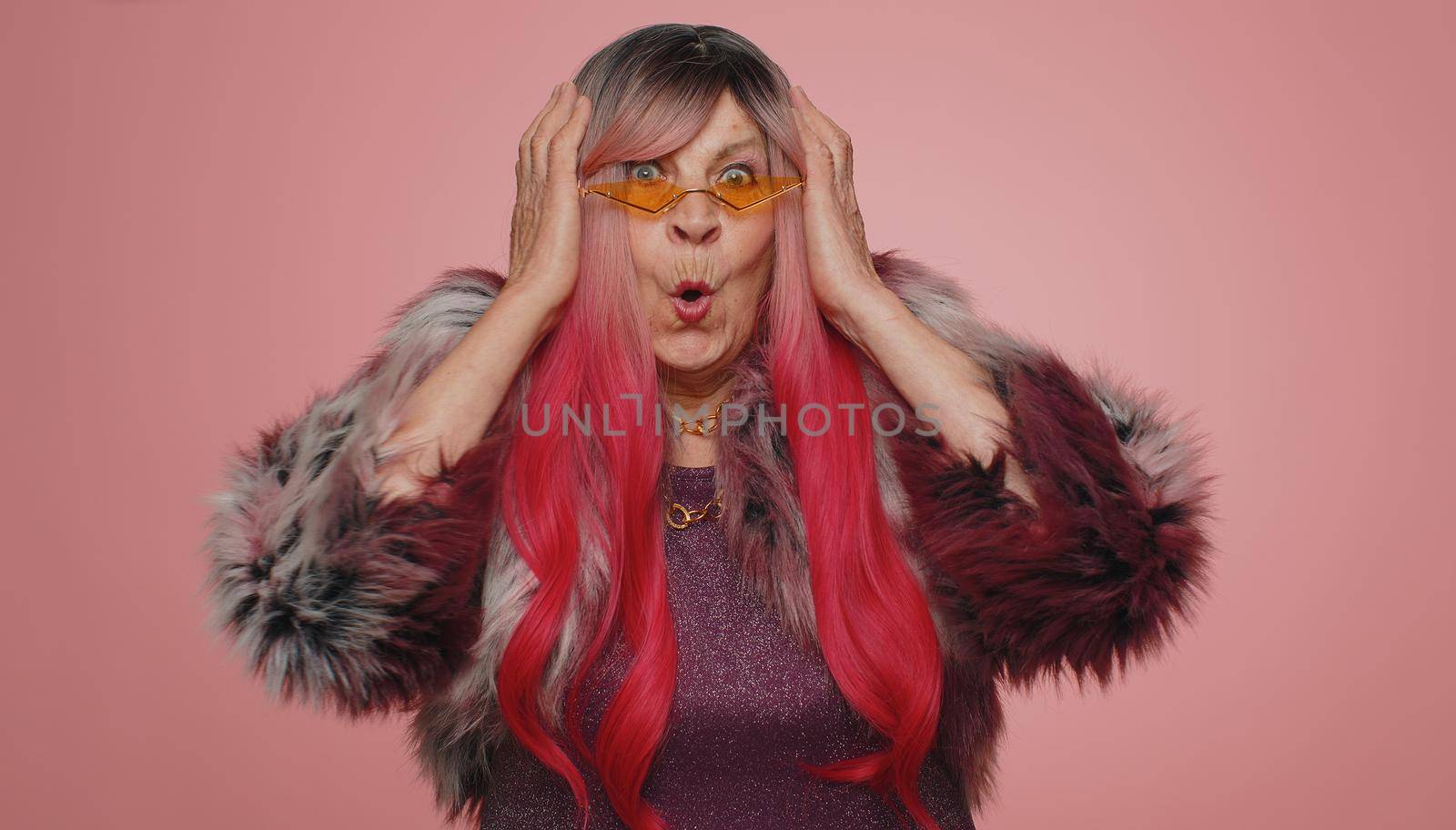 Oh my God, Wow. Excited amazed winner woman raising hands in surprise looking at camera with big eyes, shocked by sudden victory. Sincere senior elderly grandmother isolated on pink studio background