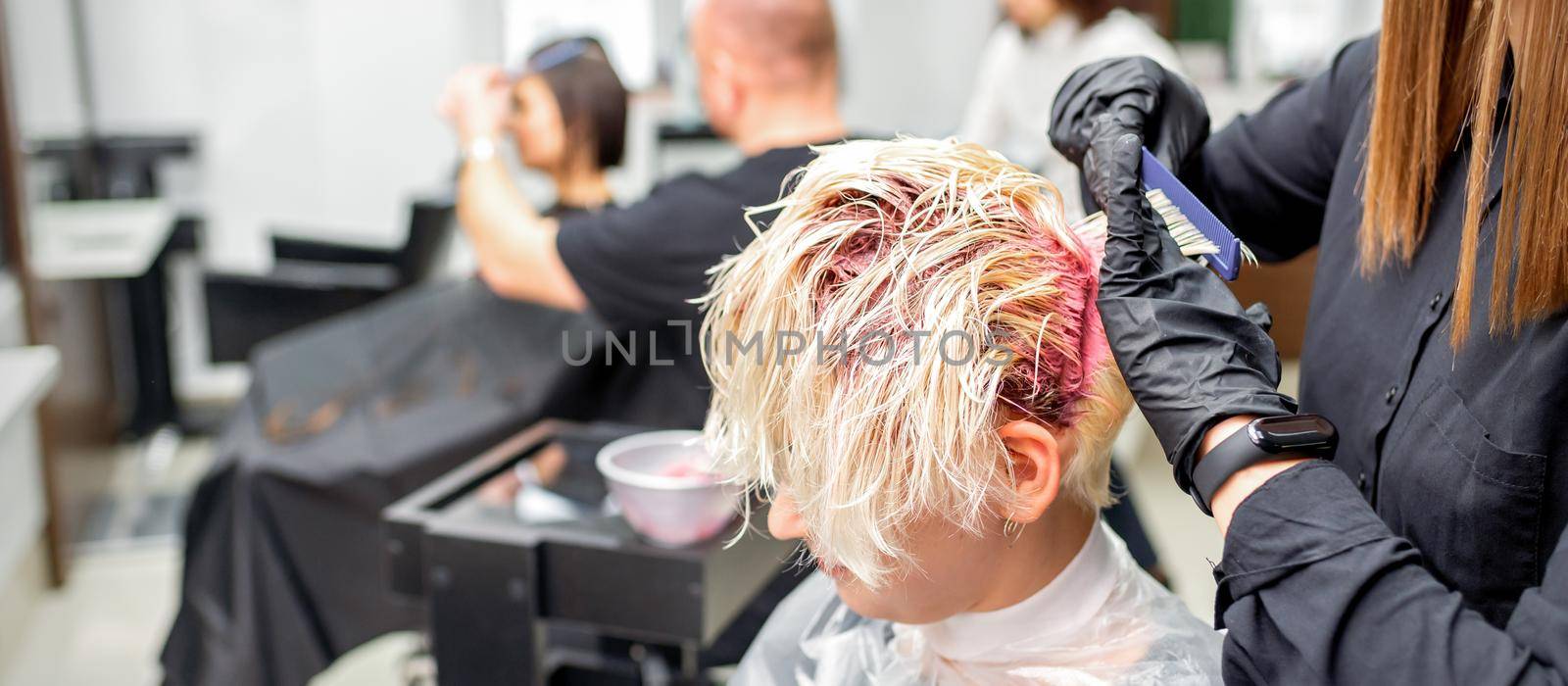 The professional hairdresser uses a brush to apply the pink dye to the hair. Hair coloring concept. by okskukuruza