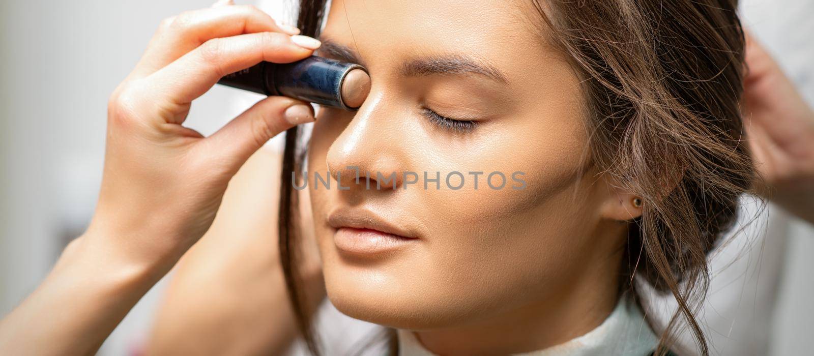 Make up artist contouring the face of a young woman with cream blush close up