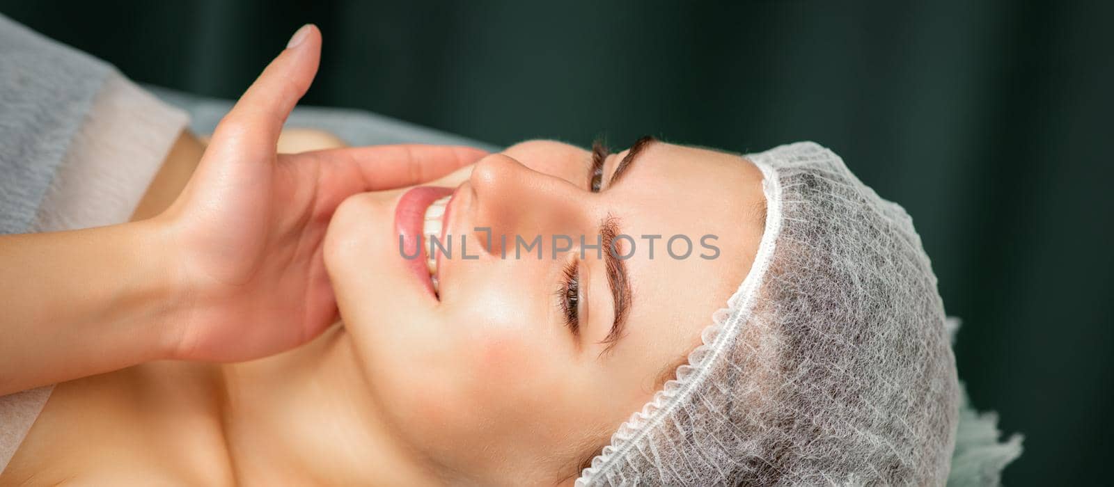 Doctor examining the beautiful face of young smiling woman in beauty clinic. by okskukuruza