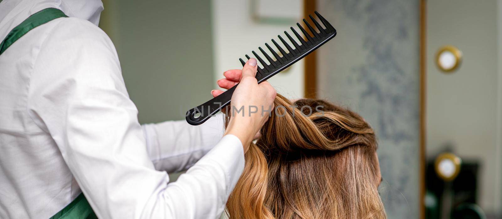 A female hairdresser is combing the long brown hair of a young woman at a parlor