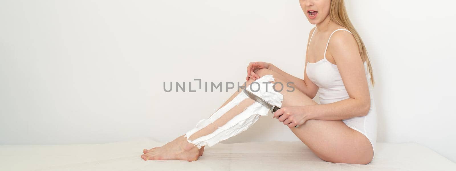 Beautiful caucasian woman shaving her legs with a knife with shaving foam on white background. Depilation and epilation concept