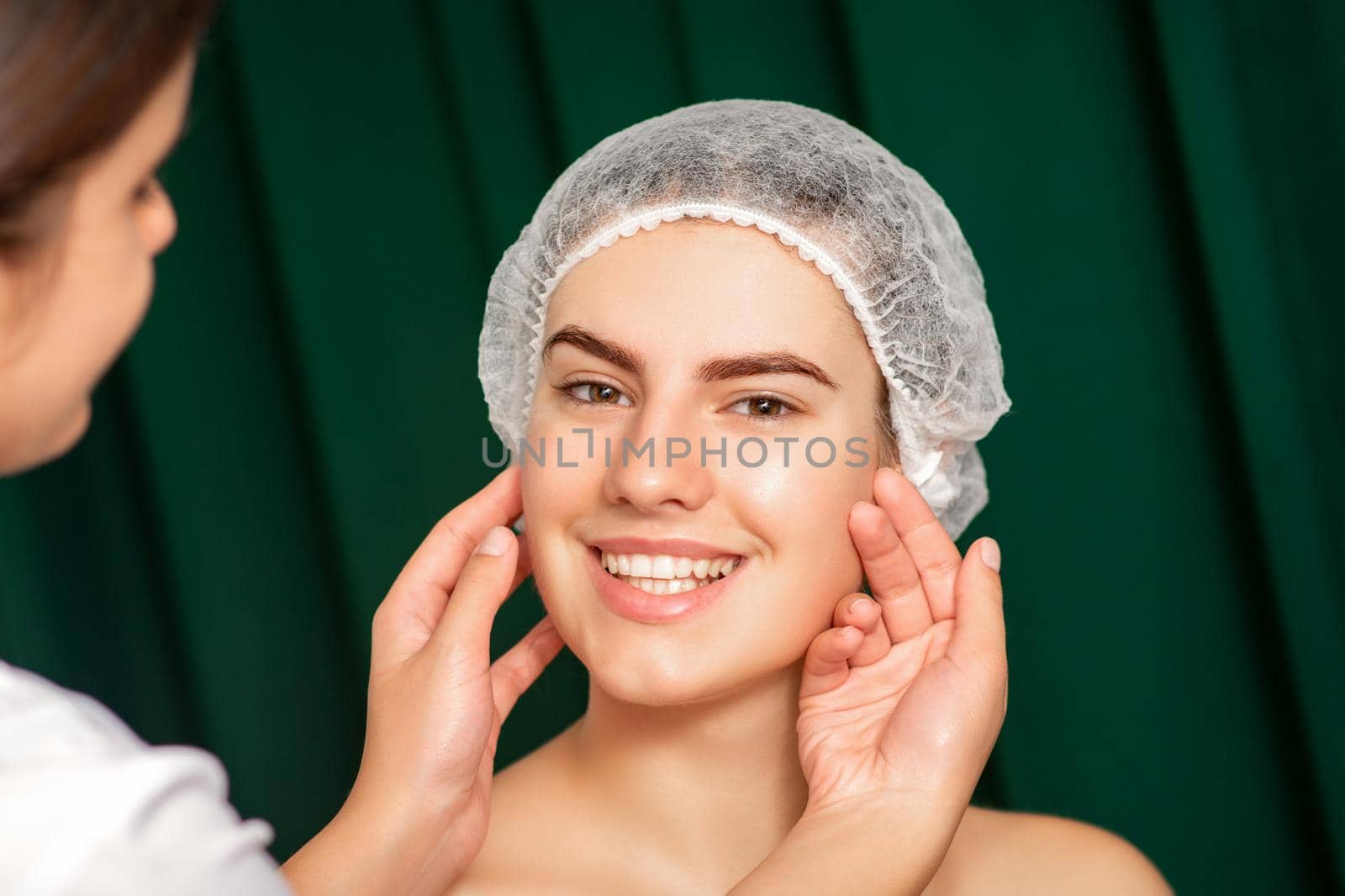 Doctor examining the beautiful face of young smiling woman in beauty clinic. by okskukuruza