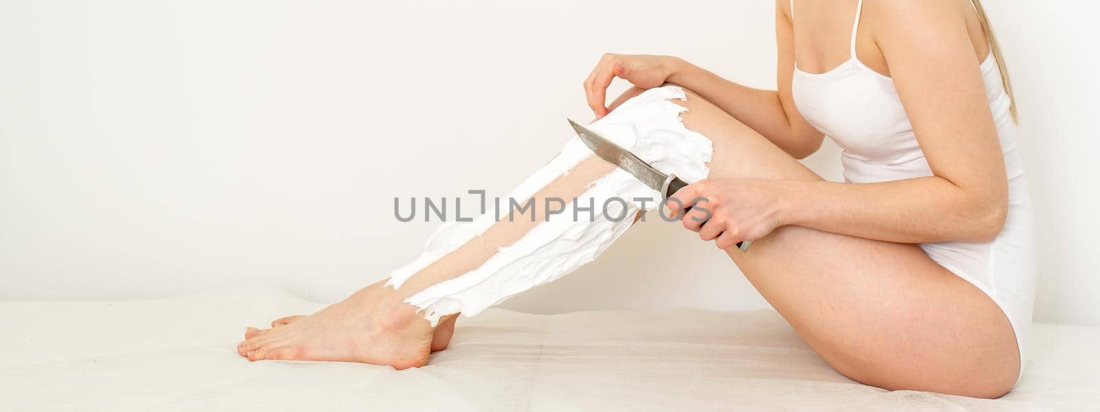 Beautiful caucasian woman shaving her legs with a knife with shaving foam on white background. Depilation and epilation concept. by okskukuruza