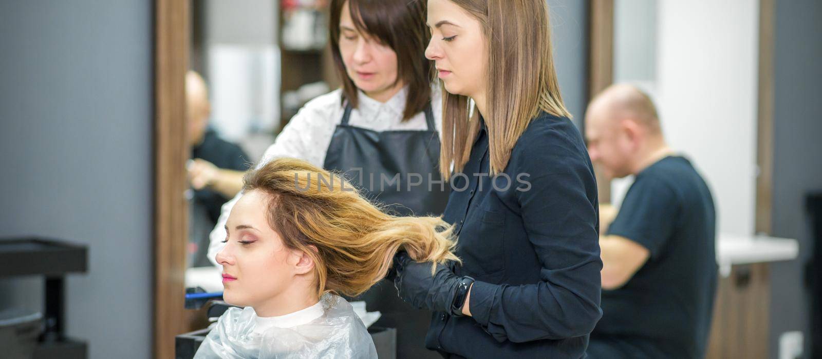 Two female hairstylists prepare long hair of a young woman making curls hairstyle in a beauty salon. by okskukuruza