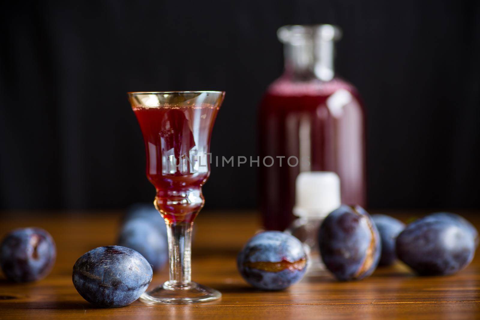 plum red wine in a glass and a decanter against the background of ripe large plums on the table.