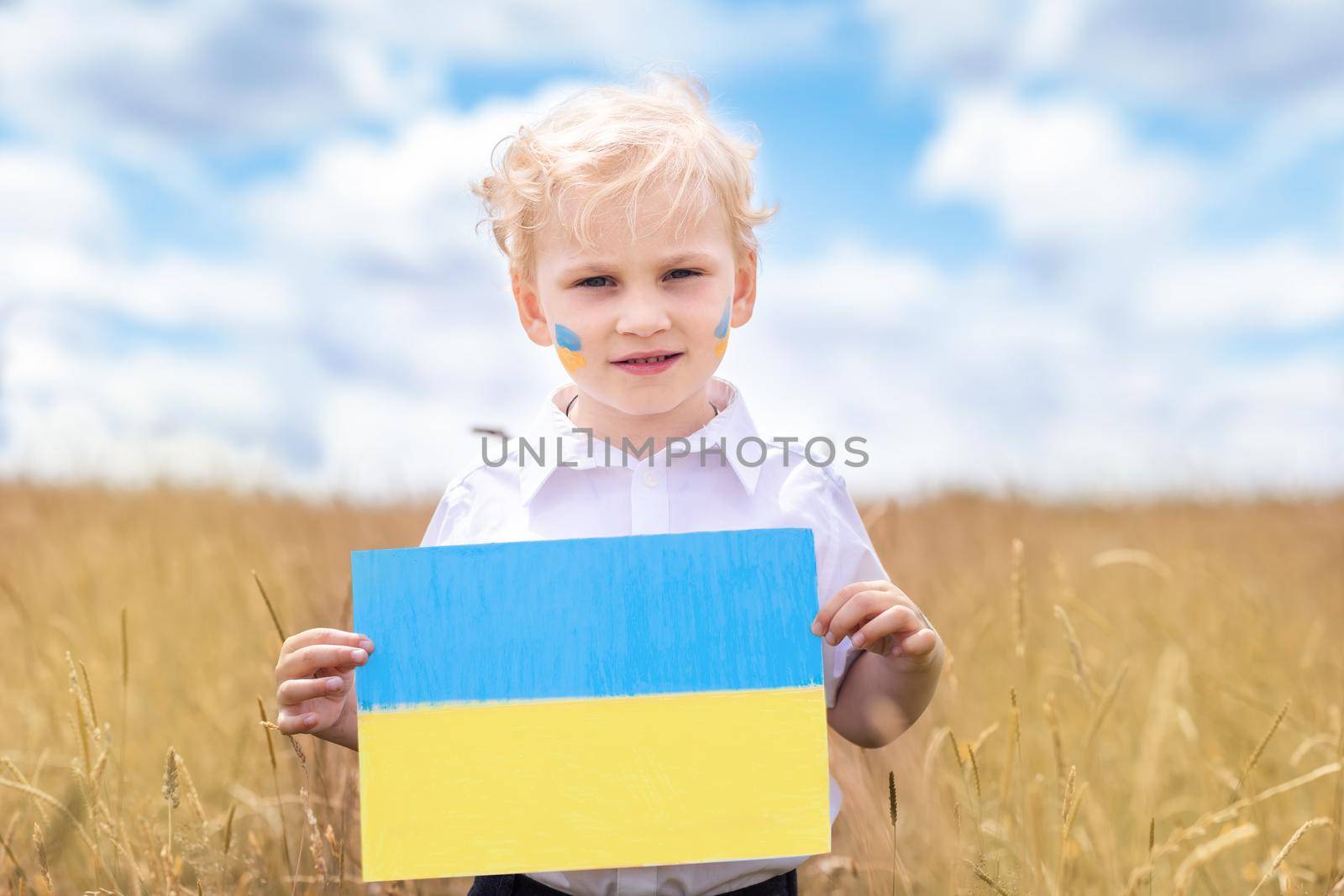 Stop War in Ukraine. Love Ukraine concept. Ukrainian boy with Ukrainina flag- yellow and blue stands in the wheat field against blue sky.