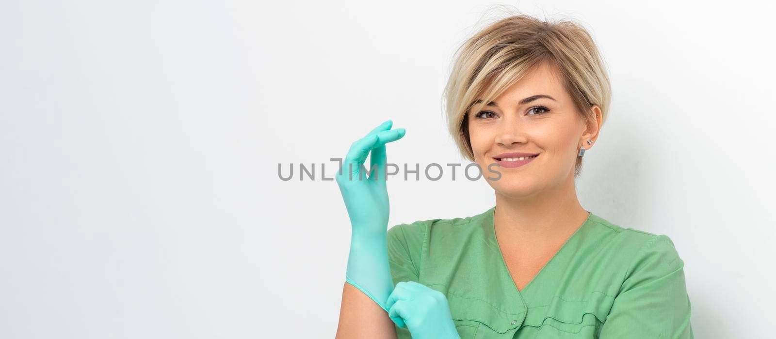 Doctor beautician puts on sterile blue gloves smiling prepares to receive clients on white