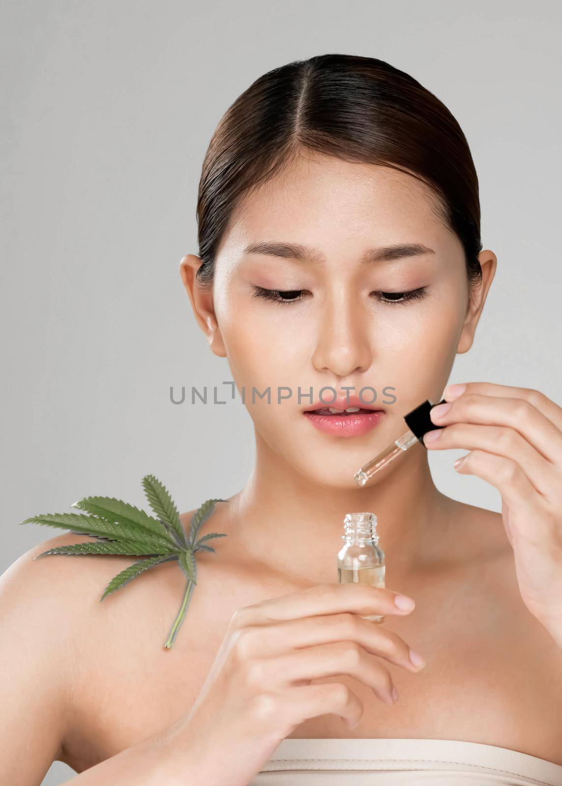 Closeup young ardent woman with healthy fresh skin holding green hemp leaf and cbd oil. Combination of beauty and cannabis concept.