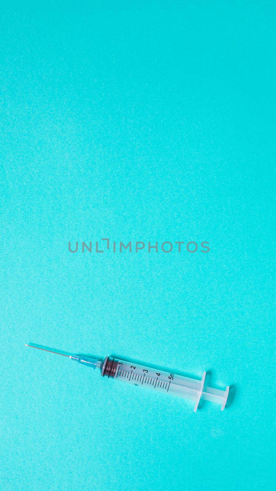 Syringe on pastel blue background from above by Ciorba