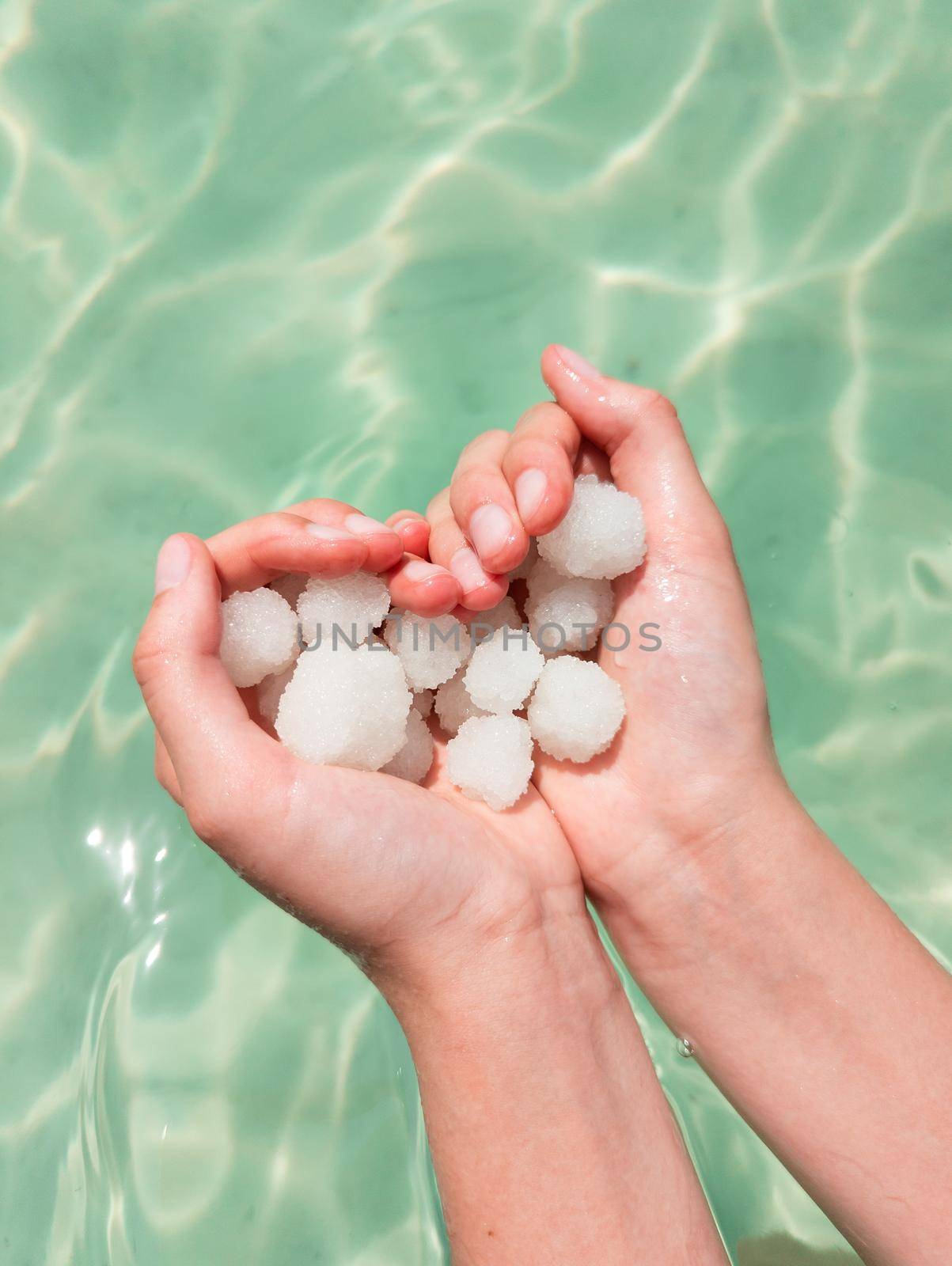 Hands holding sea salt crystals heart-saped on sea water background. Dead sea salt spa minerals cosmetic concept