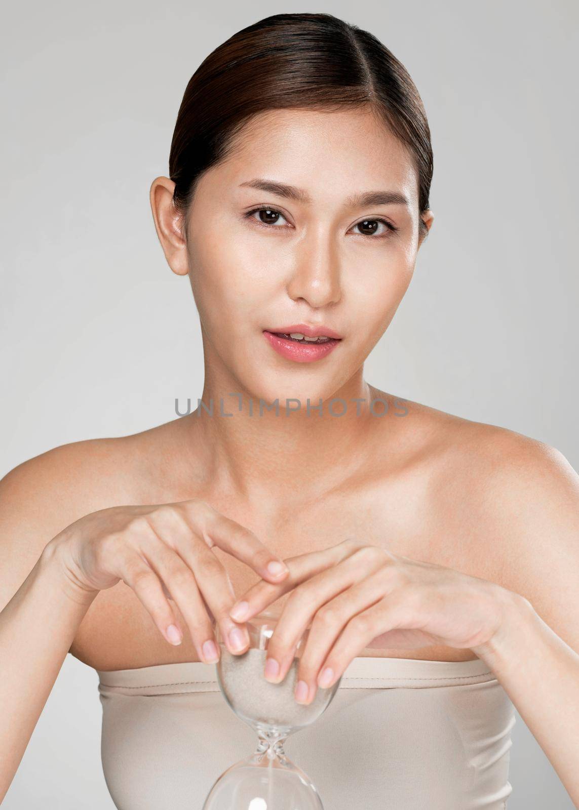 The concept of anti-aging demonstrated by closeup portrait of an ardent young woman holding an hourglass. Skincare treatment, beauty care and cosmetic ideas.