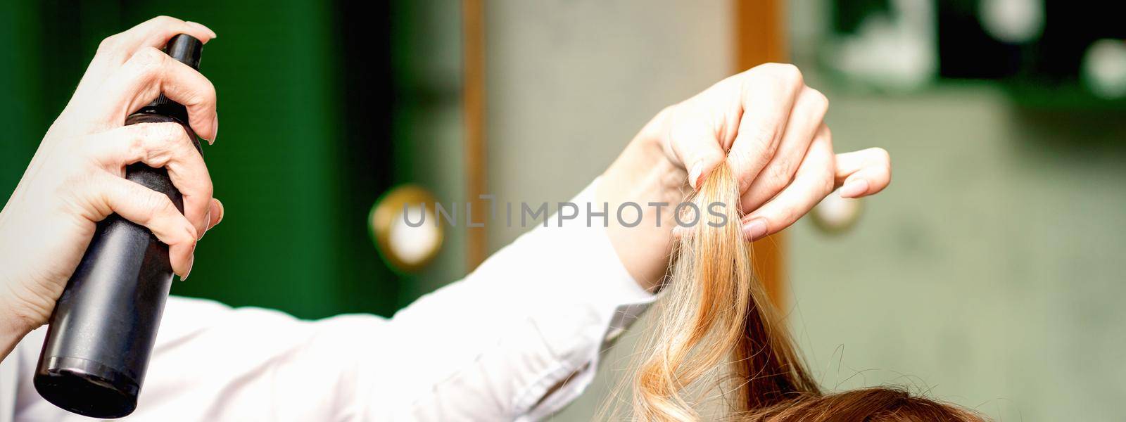 Female coiffeur fixing hairstyling of blonde woman with hairspray in a beauty salon. by okskukuruza