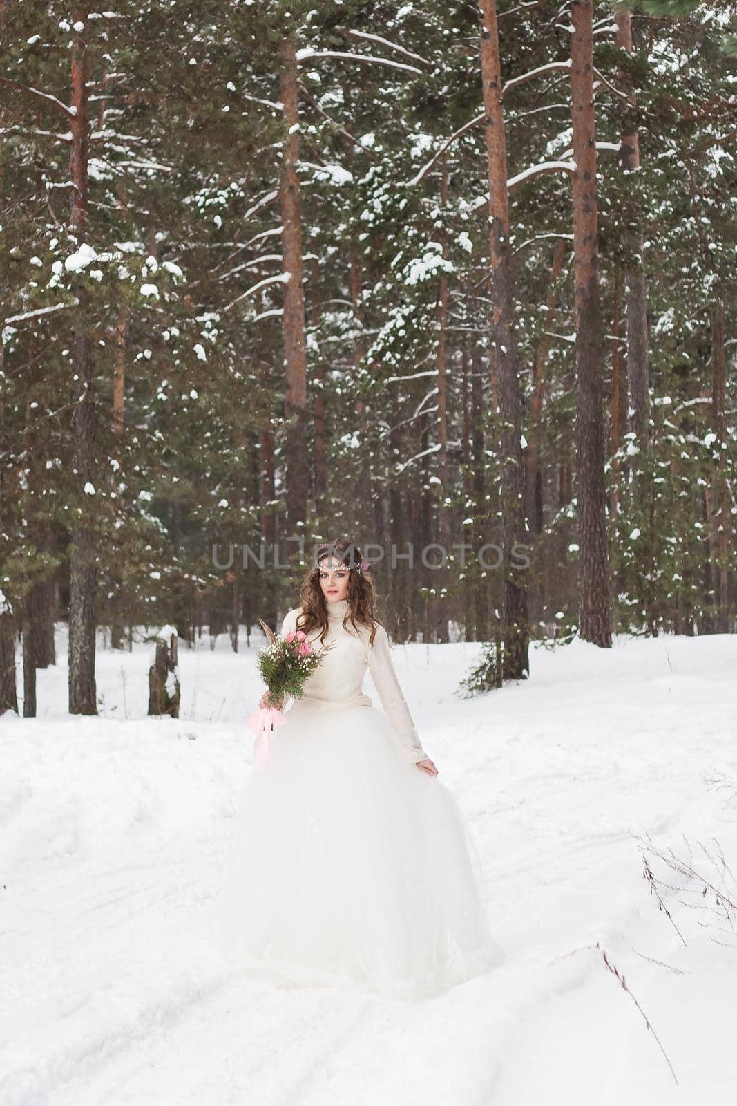 Beautiful bride in a white dress with a bouquet in a snow-covered winter forest. Portrait of the bride in nature.