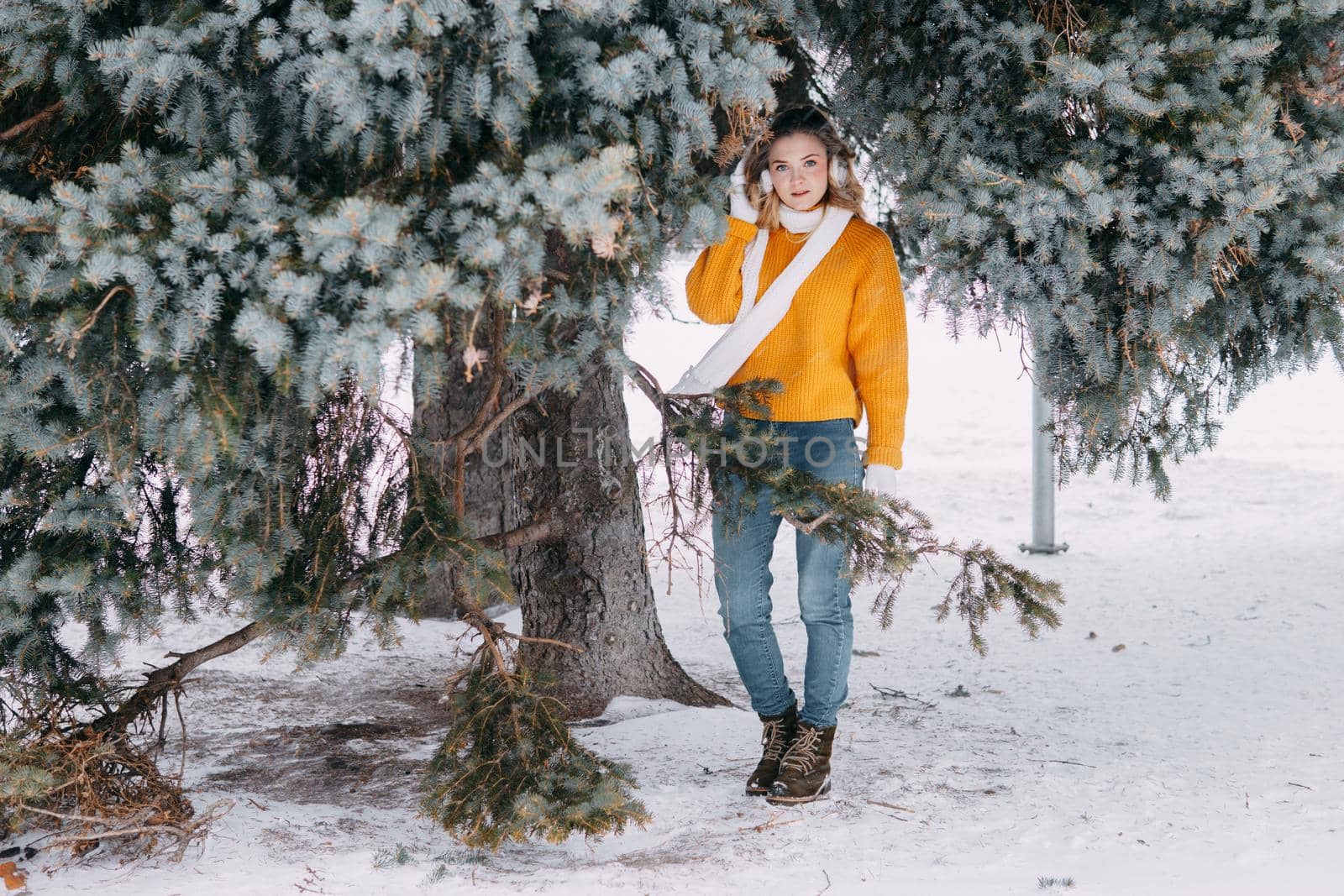 Teen blonde in a yellow sweater outside in winter. A teenage girl on a walk in winter clothes in a snowy forest.