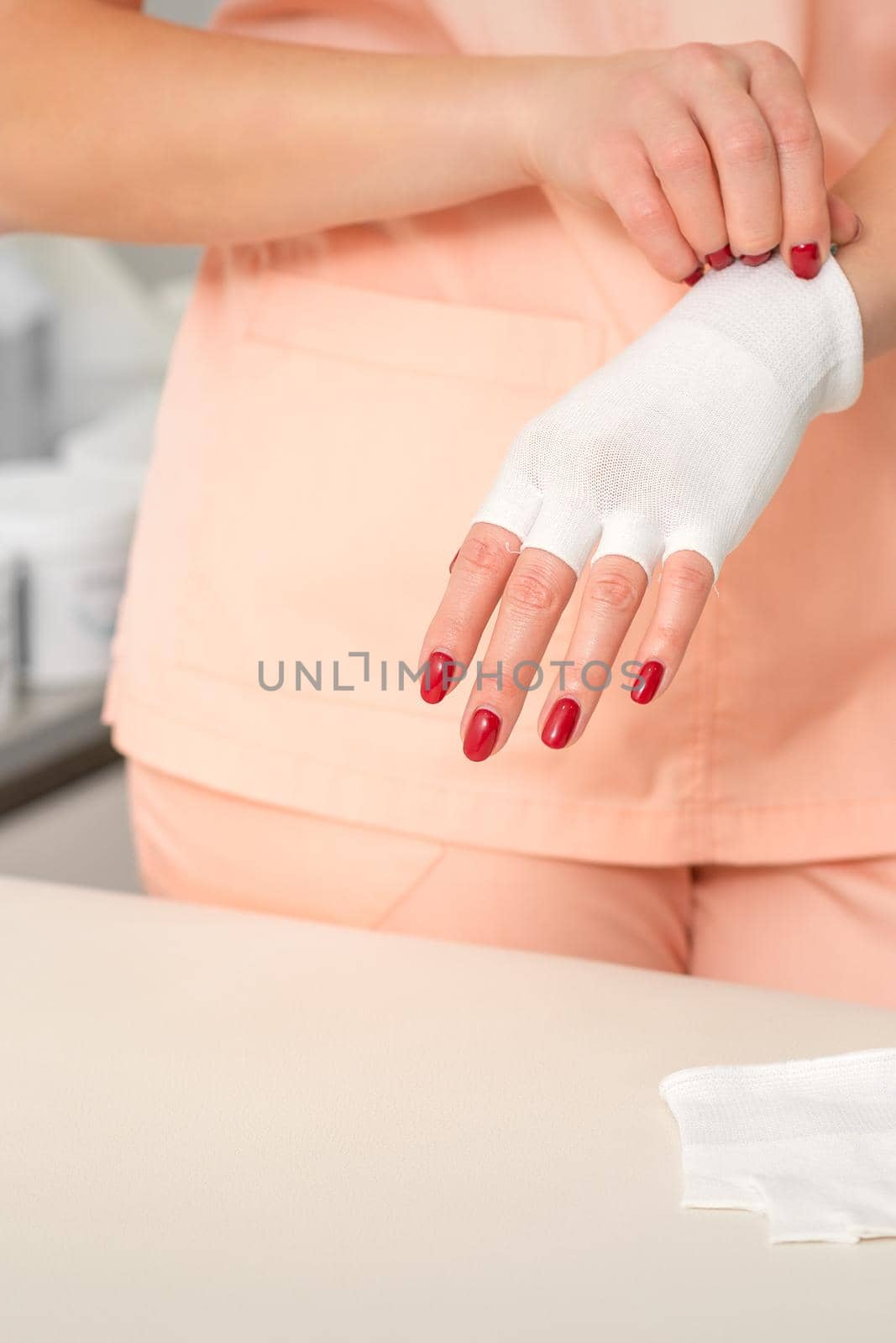 Cosmetologist in workwear wearing white bamboo fingerless gloves on her hands